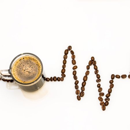 Overhead view of a cup of coffee with trail of coffee beans in shape of a heartbeat rhythm on an ECG